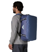 A man carrying the Patagonia black hole 40l duffel bag in current blue on his back by the shoulder straps. Backpack available at Babipur. 
