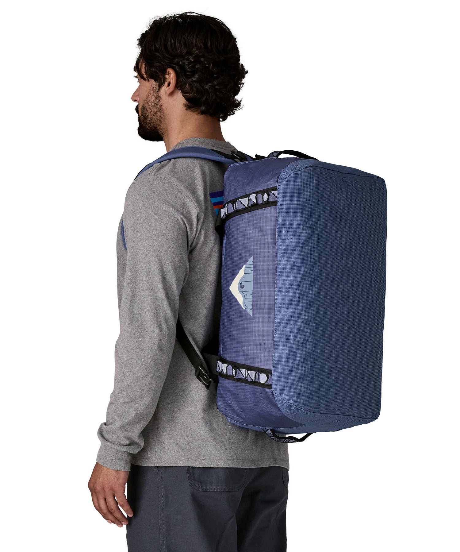 A man carrying the Patagonia black hole 40l duffel bag in current blue on his back by the shoulder straps. Backpack available at Babipur. 