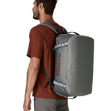 A man carrying the Patagonia black hole 40l duffel bag in noble grey on his back by the shoulder straps. Backpack available at Babipur. 