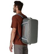 A man carrying the Patagonia black hole 40l duffel bag in noble grey on his back by the shoulder straps. Backpack available at Babipur. 