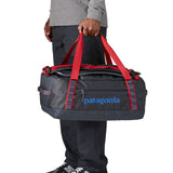A man carrying the Patagonia black hole 40l duffel bag in smolder blue / amanita red available at Babipur. 