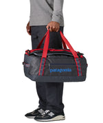 A man carrying the Patagonia black hole 40l duffel bag in smolder blue / amanita red available at Babipur. 