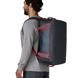 A man carrying the Patagonia black hole 40l duffel bag in smolder blue / amanita red on his back by the shoulder straps. Backpack available at Babipur. 