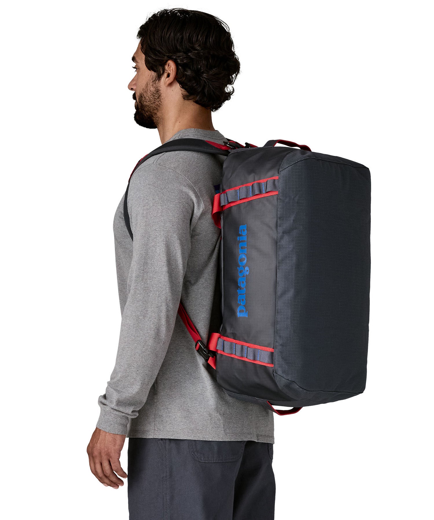 A man carrying the Patagonia black hole 40l duffel bag in smolder blue / amanita red on his back by the shoulder straps. Backpack available at Babipur. 