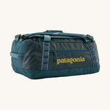 Patagonia black hole 40l duffel bag in tidal teal / luminous pink available at Babipur. A dark teal colour bag with pink trim and a mustard colour branding  on the side. Features shoulders straps and a handle on the top for easy carrying.