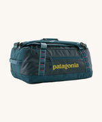 Patagonia black hole 40l duffel bag in tidal teal / luminous pink available at Babipur. A dark teal colour bag with pink trim and a mustard colour branding  on the side. Features shoulders straps and a handle on the top for easy carrying.