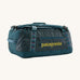 Patagonia black hole 40l duffel bag in tidal teal / luminous pink available at Babipur. A dark teal colour bag with pink trim and a mustard colour branding  on the side. Features shoulders straps and a handle on the top for easy carrying.