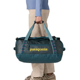 A woman carrying the Patagonia black hole 40l duffel bag in tidal teal / luminous pink available at Babipur. 