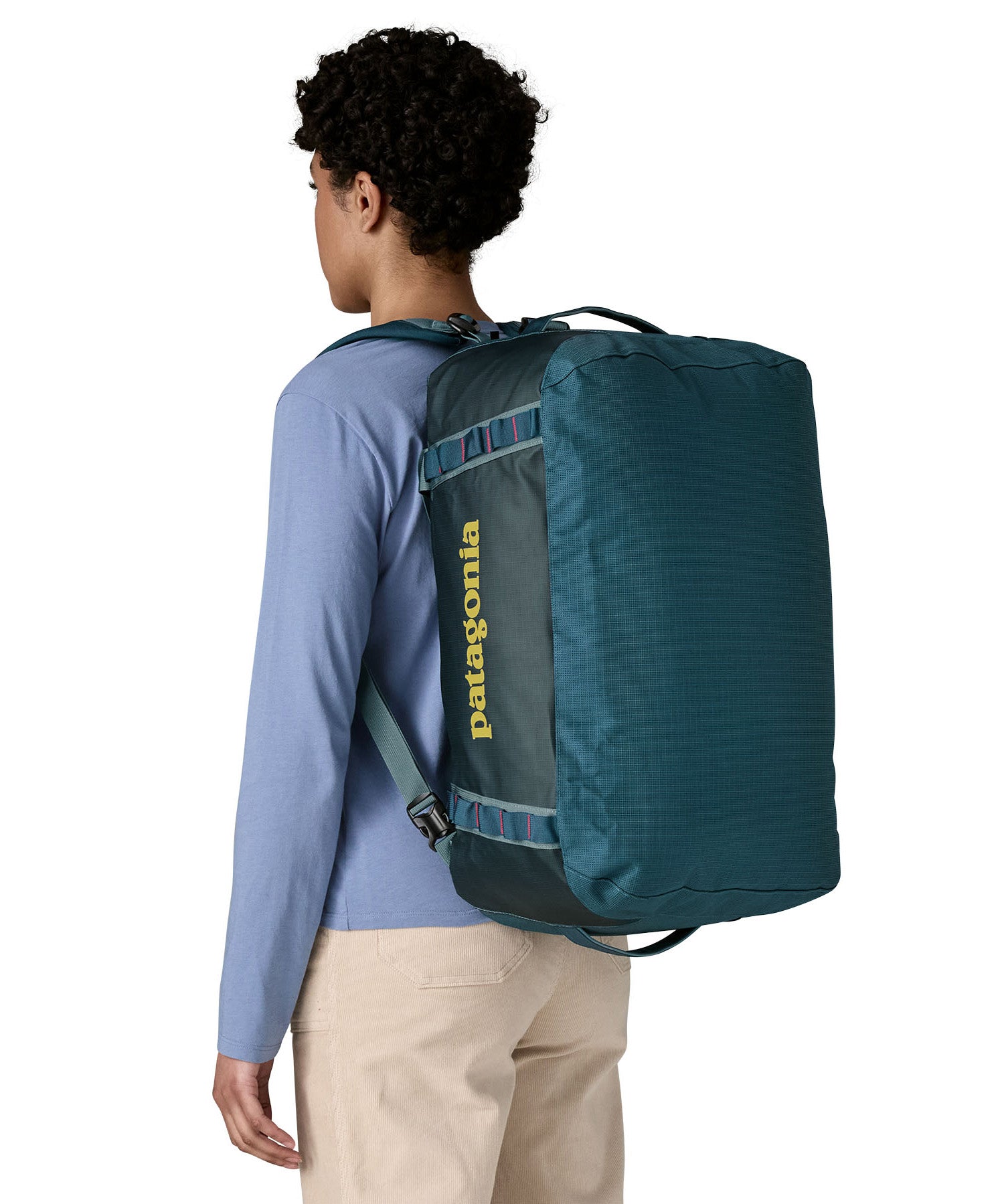 A woman carrying the Patagonia black hole 40l duffel bag in tidal teal / luminous pink on her back by the shoulder straps. Backpack available at Babipur. 