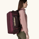 Woman carrying Patagonia Black Hole Duffel 40L in Berry Fig on her back with shoulder straps.