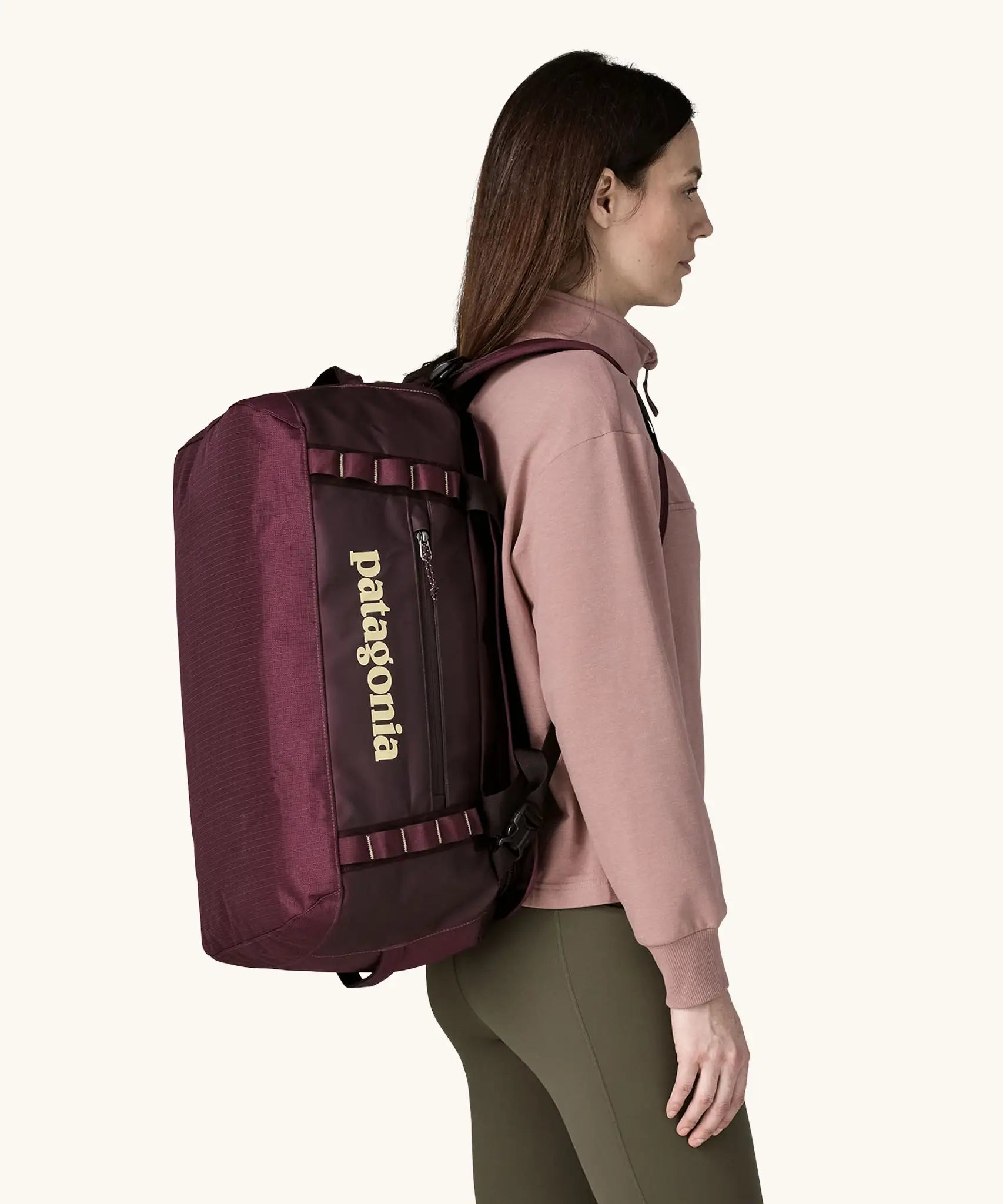 Woman carrying Patagonia Black Hole Duffel 40L in Berry Fig on her back with shoulder straps.