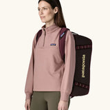 Woman carrying Patagonia Black Hole Duffel 40L in Berry Fig on her back with shoulder straps.