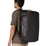 A man carrying the Patagonia black hole 55L duffel bag in black on black on his back by the shoulder straps. Backpack available at Babipur. 