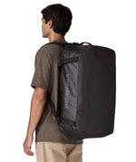 A man carrying the Patagonia black hole 55L duffel bag in black on black on his back by the shoulder straps. Backpack available at Babipur. 