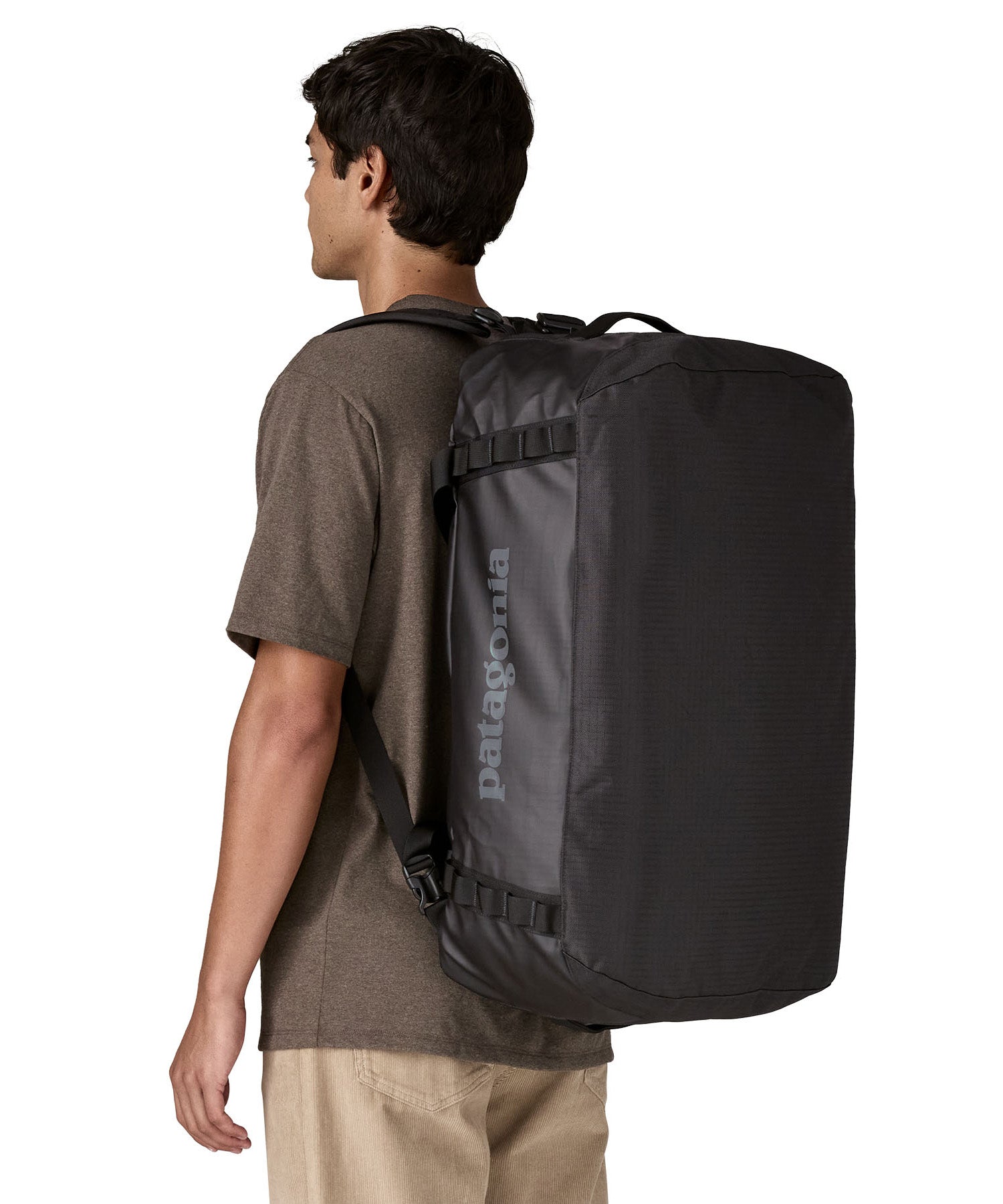 A man carrying the Patagonia black hole 55L duffel bag in black on black on his back by the shoulder straps. Backpack available at Babipur. 
