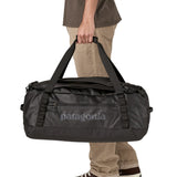 A man carrying the Patagonia black hole 55L duffel bag in black on black available at Babipur. 