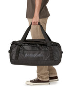 A man carrying the Patagonia black hole 55L duffel bag in black on black available at Babipur. 