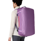 A woman carrying the Patagonia black hole 55L duffel bag in brisk purple on her back by the shoulder straps. Backpack available at Babipur. 