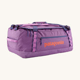 Patagonia black hole 55L duffel bag in brisk purple available at Babipur. A bright purple bag with orange branding on the side. Features shoulders straps and a handle on the top for easy carrying.