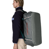 A woman carrying the Patagonia black hole 55L duffel bag in noble grey on her back by the shoulder straps. Backpack available at Babipur. 