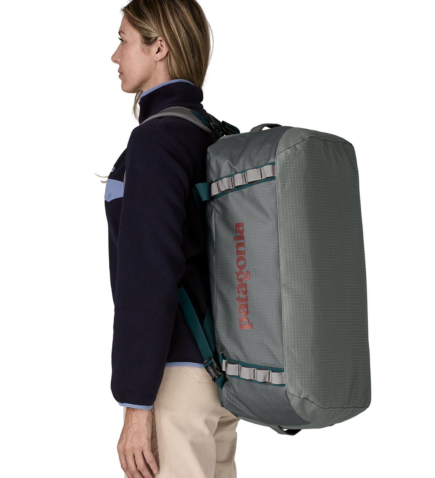 Woman carrying the Patagonia black hole 55L duffel bag in noble grey on her back by the shoulder straps. 