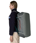 A woman carrying the Patagonia black hole 55L duffel bag in noble grey on her back by the shoulder straps. Backpack available at Babipur. 