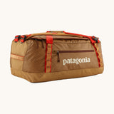 Patagonia black hole 55L duffel bag in talon gold available at Babipur. A dark yellow colour bag with red trim and a cream colour branding  on the side. Features shoulders straps and a handle on the top for easy carrying.