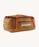 Patagonia black hole 55L duffel bag in talon gold available at Babipur. A dark yellow colour bag with red trim and a cream colour branding  on the side. Features shoulders straps and a handle on the top for easy carrying.