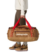 A woman carrying the Patagonia black hole 55L duffel bag in talon gold available at Babipur. 