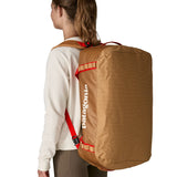 A woman carrying the Patagonia black hole 55L duffel bag in talon gold on her back by the shoulder straps. Backpack available at Babipur. 