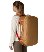A woman carrying the Patagonia black hole 55L duffel bag in talon gold on her back by the shoulder straps. Backpack available at Babipur. 