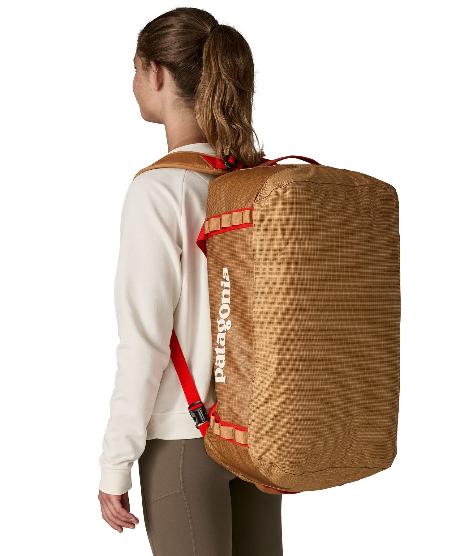 A woman carrying the Patagonia black hole 55L duffel bag in talon gold on her back by the shoulder straps. Backpack available at Babipur. 