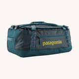 Patagonia black hole 55L duffel bag in tidal teal / luminous pink available at Babipur. A dark teal colour bag with pink trim and a mustard colour branding  on the side. Features shoulders straps and a handle on the top for easy carrying.