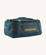 Patagonia black hole 55L duffel bag in tidal teal / luminous pink available at Babipur. A dark teal colour bag with pink trim and a mustard colour branding  on the side. Features shoulders straps and a handle on the top for easy carrying.