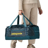 A woman carrying the Patagonia black hole 55L duffel bag in tidal teal / luminous pink available at Babipur. 