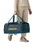 A woman carrying the Patagonia black hole 55L duffel bag in tidal teal / luminous pink available at Babipur. 