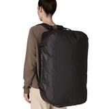 A woman carrying the Patagonia black hole 70L duffel bag in black on black on her back by the shoulder straps. Backpack available at Babipur. 