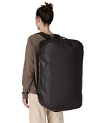 A woman carrying the Patagonia black hole 70L duffel bag in black on black on her back by the shoulder straps. Backpack available at Babipur. 