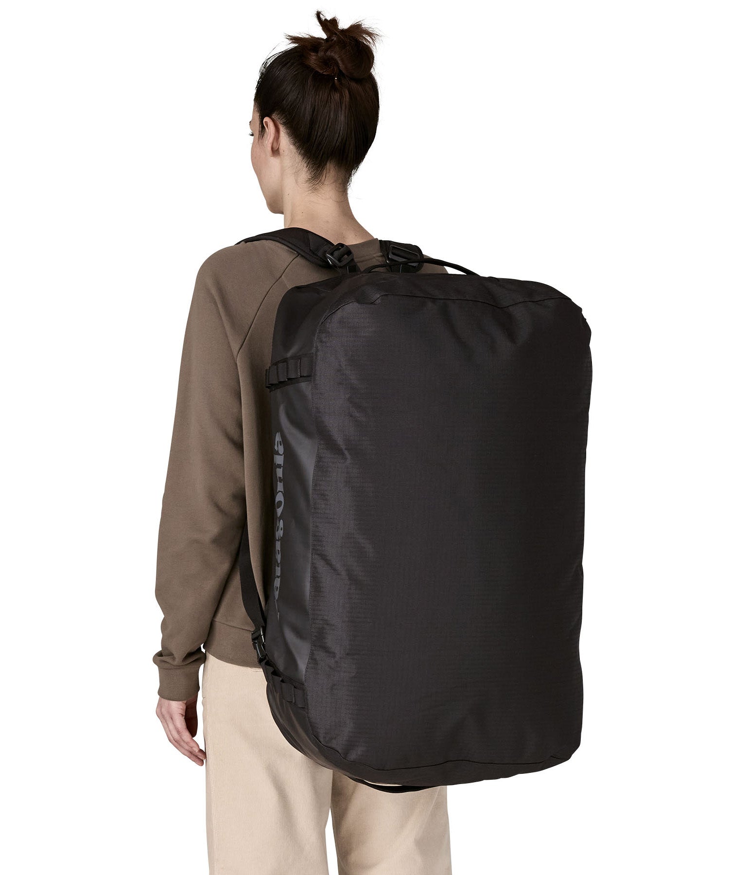 A woman carrying the Patagonia black hole 70L duffel bag in black on black on her back by the shoulder straps. Backpack available at Babipur. 