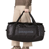 A woman carrying the Patagonia black hole 70L duffel bag in black on black available at Babipur. 