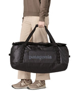 A woman carrying the Patagonia black hole 70L duffel bag in black on black available at Babipur. 