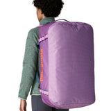 A woman carrying the Patagonia black hole 70L duffel bag in brisk purple on her back by the shoulder straps. Backpack available at Babipur. 