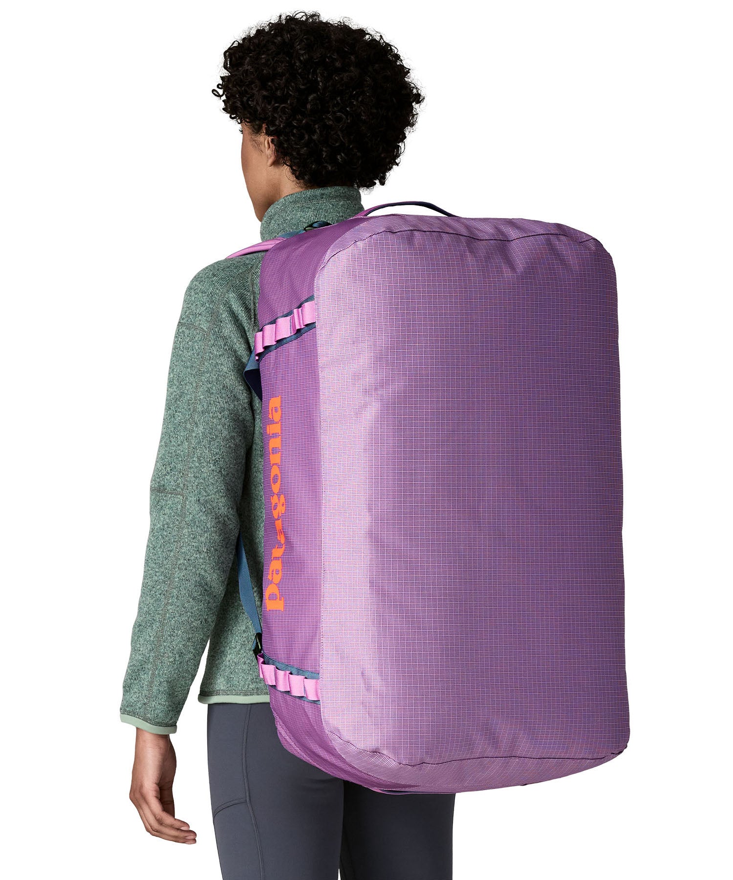 A woman carrying the Patagonia black hole 70L duffel bag in brisk purple on her back by the shoulder straps. Backpack available at Babipur. 