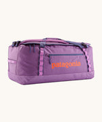 Patagonia black hole 70L duffel bag in brisk purple available at Babipur. A bright purple bag with orange branding on the side. Features shoulders straps and a handle on the top for easy carrying.