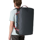 A man carrying the Patagonia black hole 70L duffel bag in smolder blue / amanita red on his back by the shoulder straps. Backpack available at Babipur. 