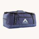 Patagonia black hole 70L duffel bag in current blue available at Babipur. A blue bag with black trim and a mountain graphic on the side. Features shoulders straps and a handle on the top for easy carrying.