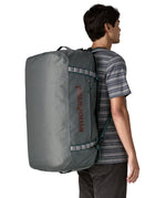 A woman carrying the Patagonia black hole 70L duffel bag in noble grey on her back by the shoulder straps. Backpack available at Babipur. 
