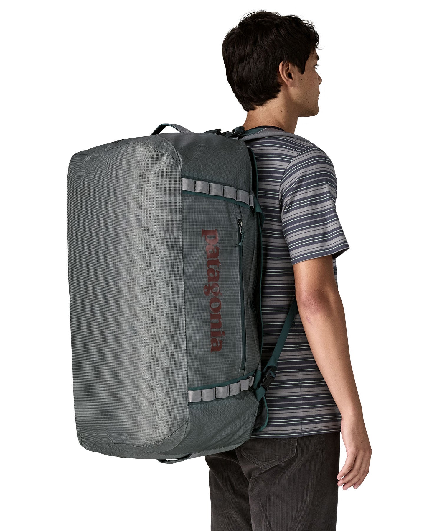 A woman carrying the Patagonia black hole 70L duffel bag in noble grey on her back by the shoulder straps. Backpack available at Babipur. 