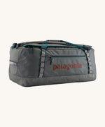 Patagonia black hole 70L duffel bag in noble grey available at Babipur. A dark grey bag with green trim and brown branding on the side. Features shoulders straps and a handle on the top for easy carrying.
