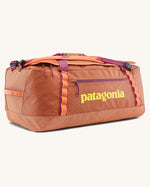 Patagonia black hole 70l duffel bag in bright orange with purple zip details, straps and yellow printed logo on front panel 